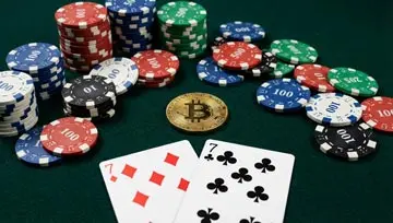 un bitcoin posé sur une table de jeu de casino, avec des jetons de casino et une paire de 7 